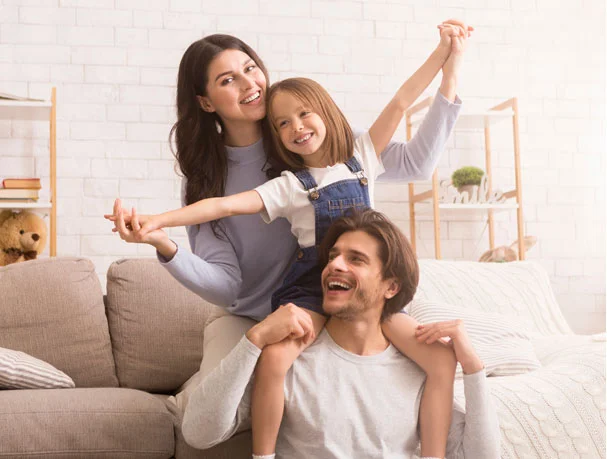 Happy family of three laughing together in a bright modern living room.
