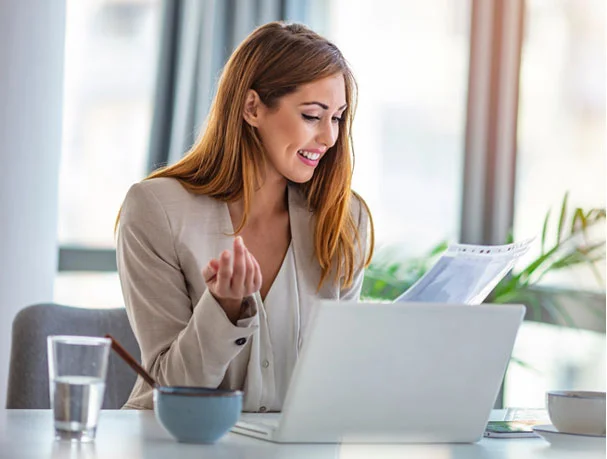 Professional woman reviewing documents on a white laptop in a bright modern workspace.